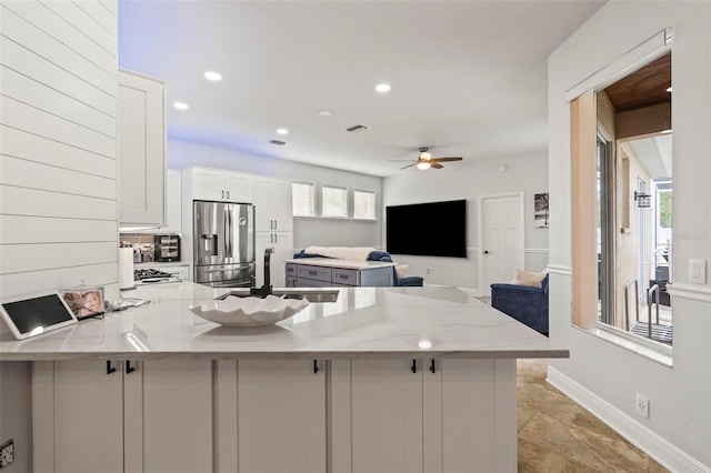 kitchen with light stone counters, white cabinetry, a sink, a peninsula, and stainless steel fridge with ice dispenser