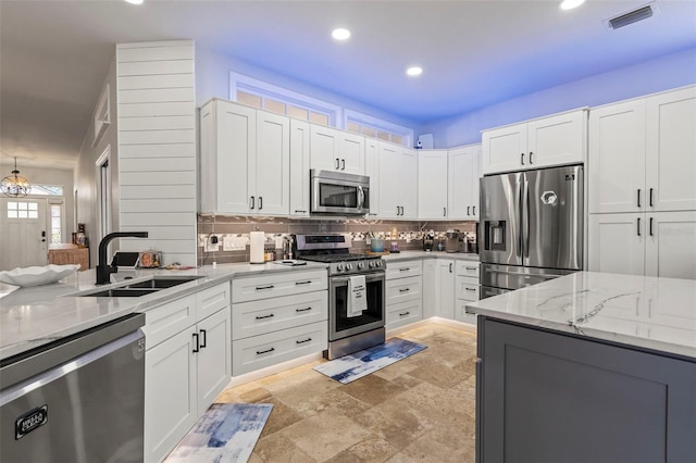 kitchen with a sink, visible vents, appliances with stainless steel finishes, backsplash, and light stone countertops