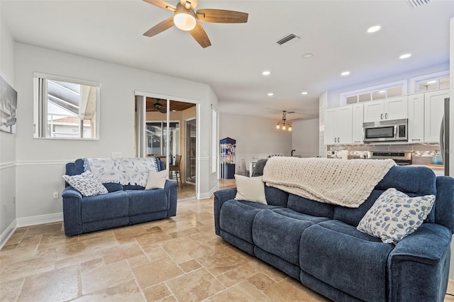 living room featuring stone tile floors, recessed lighting, visible vents, baseboards, and ceiling fan with notable chandelier