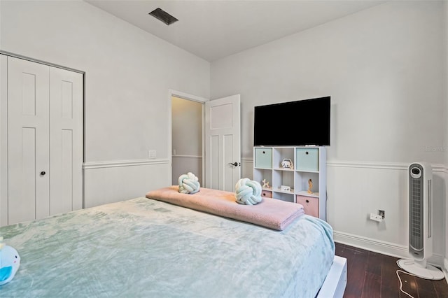 bedroom featuring a wainscoted wall, dark wood-type flooring, and a closet