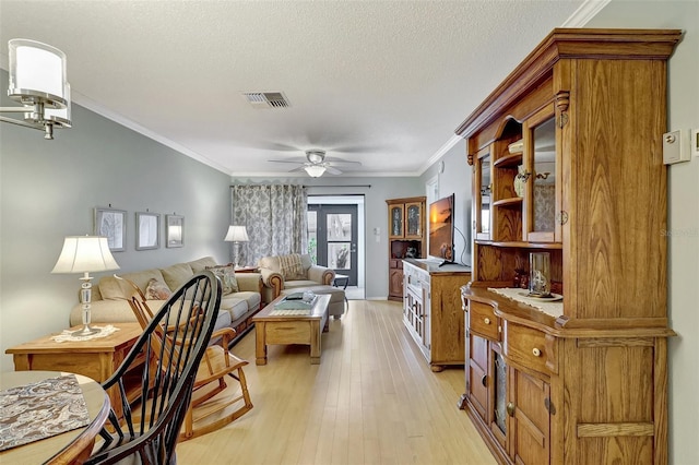 living room featuring ceiling fan, a textured ceiling, visible vents, ornamental molding, and light wood finished floors