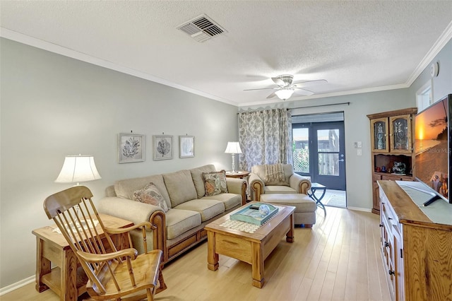 living area featuring a textured ceiling, ornamental molding, light wood-type flooring, and visible vents