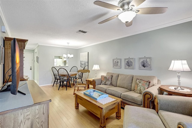 living area featuring visible vents, light wood-style flooring, ornamental molding, a textured ceiling, and ceiling fan with notable chandelier