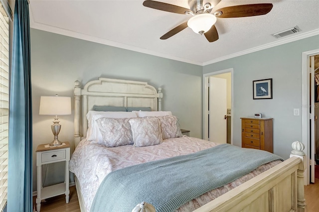 bedroom with ceiling fan, wood finished floors, visible vents, and crown molding