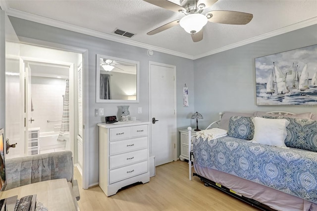 bedroom featuring ceiling fan, visible vents, light wood-type flooring, ensuite bath, and crown molding