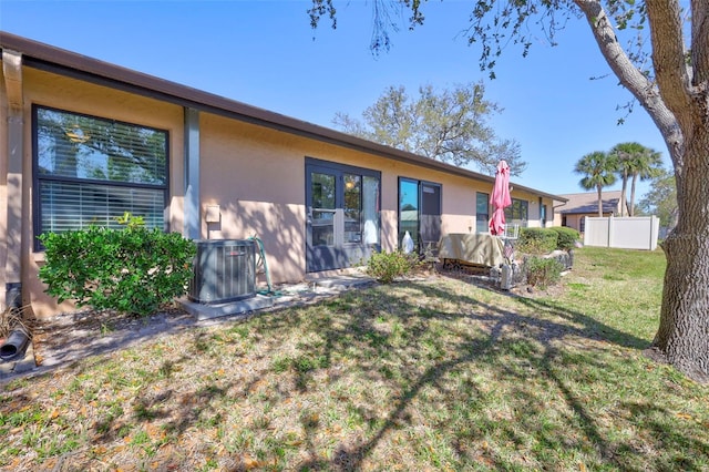 rear view of house featuring a yard, cooling unit, fence, and stucco siding