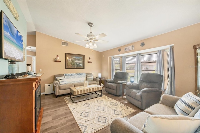 living room featuring light wood-style floors, visible vents, vaulted ceiling, and a ceiling fan