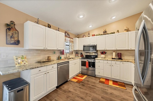 kitchen featuring lofted ceiling, appliances with stainless steel finishes, white cabinetry, a sink, and wood finished floors