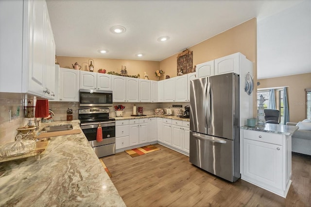 kitchen with light wood finished floors, appliances with stainless steel finishes, a sink, and decorative backsplash