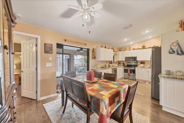 dining area with ceiling fan, light wood-style flooring, visible vents, baseboards, and vaulted ceiling