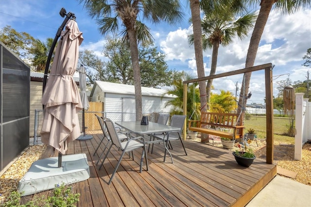 wooden terrace featuring outdoor dining space, fence, and an outdoor structure