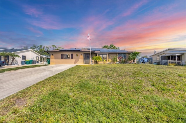 view of front of home with a yard, stucco siding, concrete driveway, roof mounted solar panels, and fence