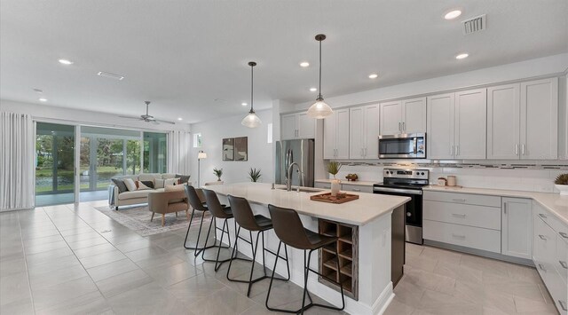 kitchen featuring a center island with sink, a breakfast bar, stainless steel appliances, open floor plan, and backsplash