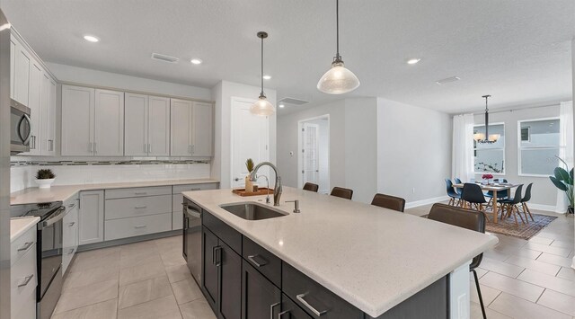 kitchen with a breakfast bar, an island with sink, a sink, appliances with stainless steel finishes, and tasteful backsplash