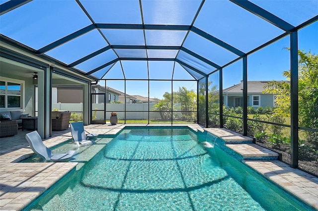 pool with glass enclosure, a patio, ceiling fan, and an outdoor hangout area