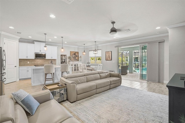 living room with light wood-type flooring, visible vents, a ceiling fan, and crown molding