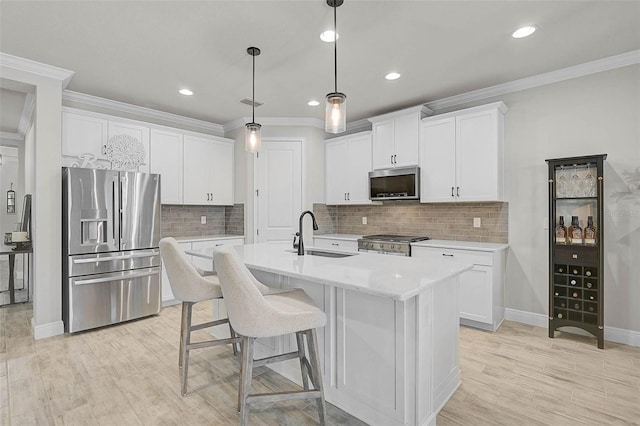 kitchen with a kitchen island with sink, a sink, light countertops, white cabinets, and appliances with stainless steel finishes