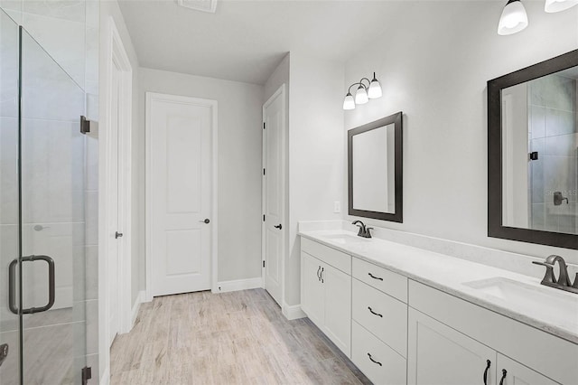 full bath with double vanity, a stall shower, wood finished floors, and a sink