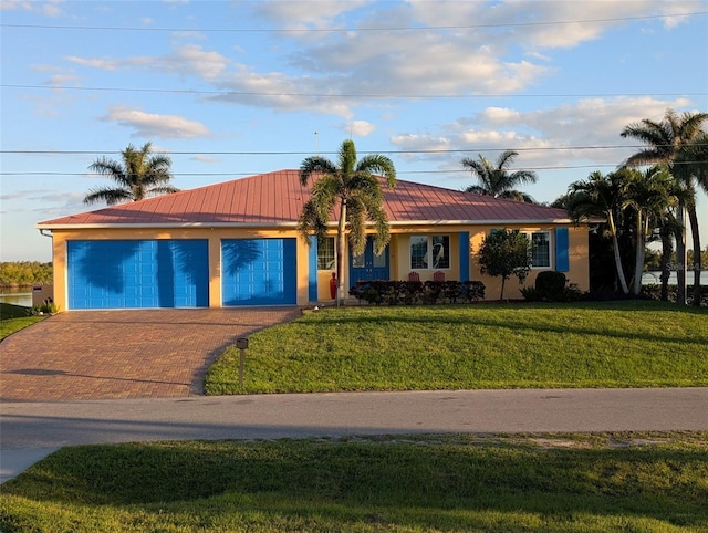 ranch-style house featuring decorative driveway, metal roof, a front lawn, and stucco siding