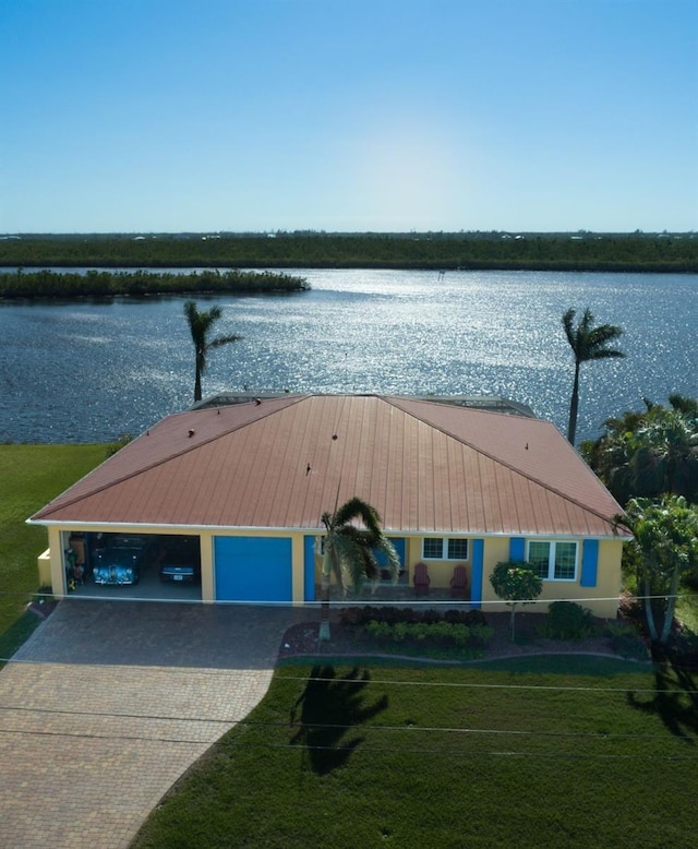 exterior space with metal roof, a water view, an attached garage, decorative driveway, and a front lawn