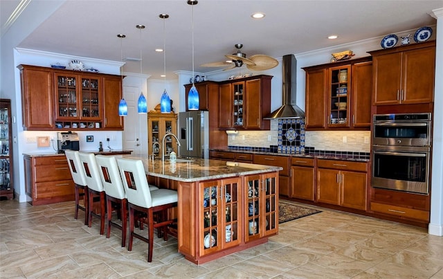 kitchen with wall chimney range hood, appliances with stainless steel finishes, and brown cabinetry