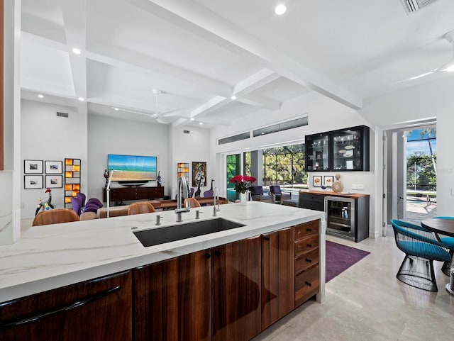 kitchen with recessed lighting, beverage cooler, a sink, beam ceiling, and glass insert cabinets