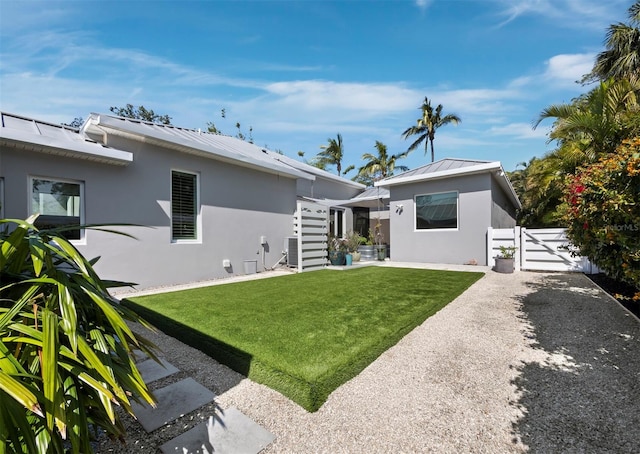 back of property with metal roof, a yard, a gate, and stucco siding