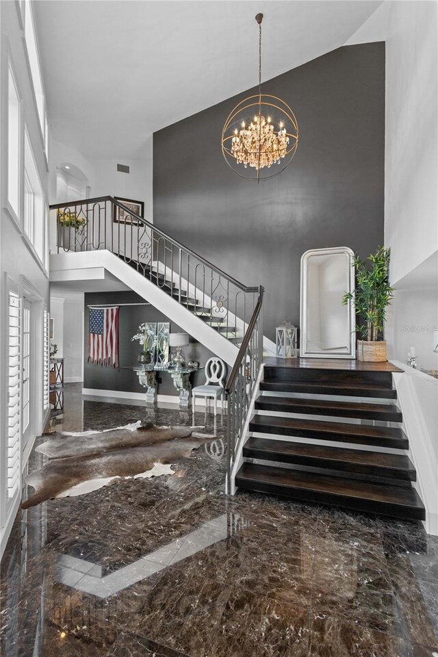 staircase with a notable chandelier, visible vents, marble finish floor, and a towering ceiling