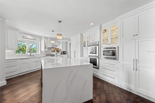 kitchen with a center island, glass insert cabinets, dark wood finished floors, appliances with stainless steel finishes, and white cabinets