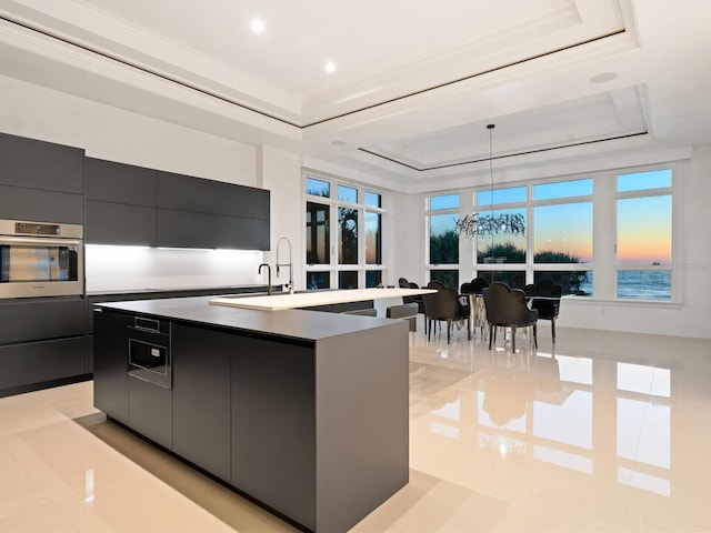 kitchen featuring dark cabinetry, a center island with sink, stainless steel oven, modern cabinets, and a raised ceiling