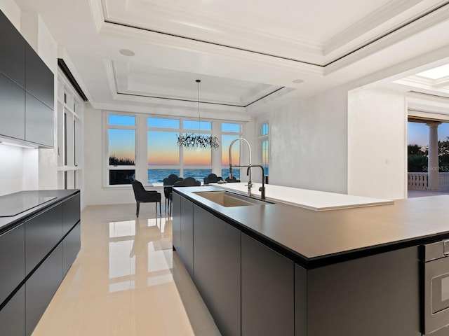 kitchen featuring a sink, a raised ceiling, modern cabinets, and a center island with sink