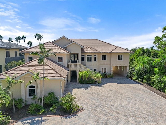 view of front of home featuring a tile roof, stairway, decorative driveway, stucco siding, and a carport