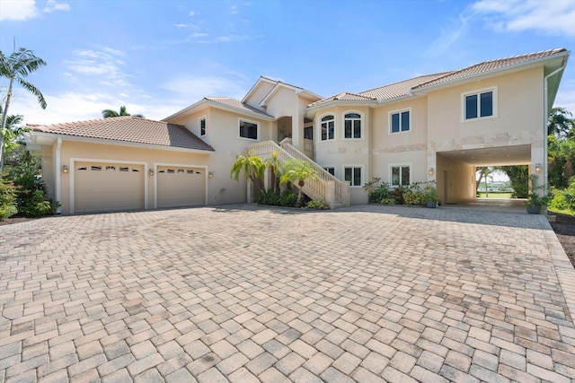 mediterranean / spanish house featuring a garage, a tiled roof, stairway, and decorative driveway