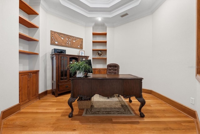 office space featuring visible vents, built in features, a tray ceiling, crown molding, and light wood-type flooring