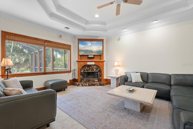 living area featuring visible vents, ceiling fan, ornamental molding, a tray ceiling, and a fireplace