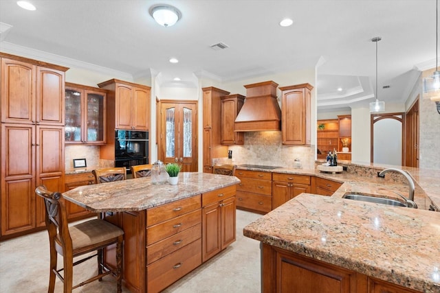 kitchen featuring premium range hood, a sink, light stone countertops, black appliances, and a kitchen bar