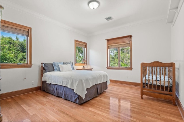 bedroom featuring baseboards, light wood-style flooring, visible vents, and crown molding