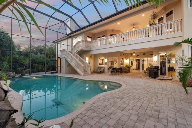 pool at dusk featuring an outdoor pool, a patio, glass enclosure, ceiling fan, and stairway