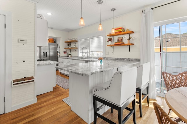 kitchen with light wood-style flooring, a peninsula, a kitchen bar, and open shelves