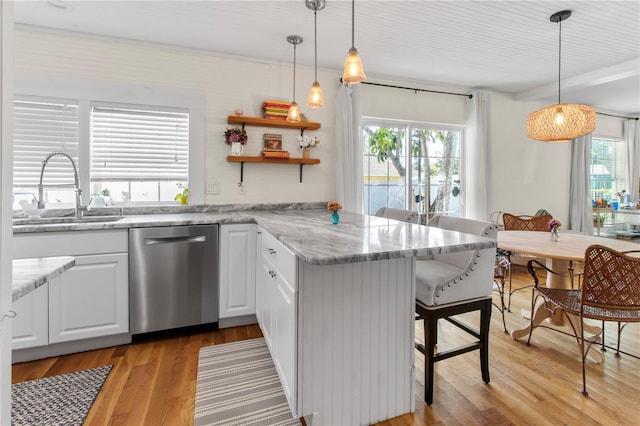 kitchen featuring a peninsula, a sink, stainless steel dishwasher, light wood finished floors, and a kitchen bar