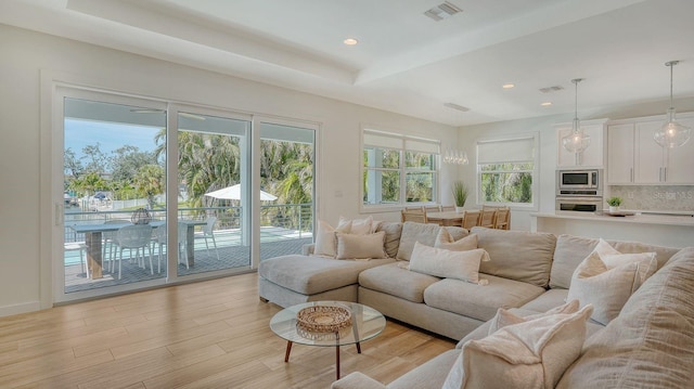 living area with a tray ceiling, light wood-style floors, visible vents, and a wealth of natural light