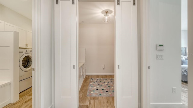 laundry room featuring a barn door, cabinet space, light wood finished floors, and washer / dryer