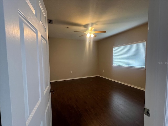 unfurnished room featuring dark wood-type flooring, visible vents, ceiling fan, and baseboards