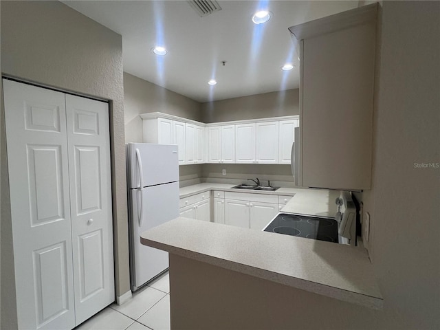 kitchen featuring light tile patterned floors, visible vents, freestanding refrigerator, range, and a peninsula