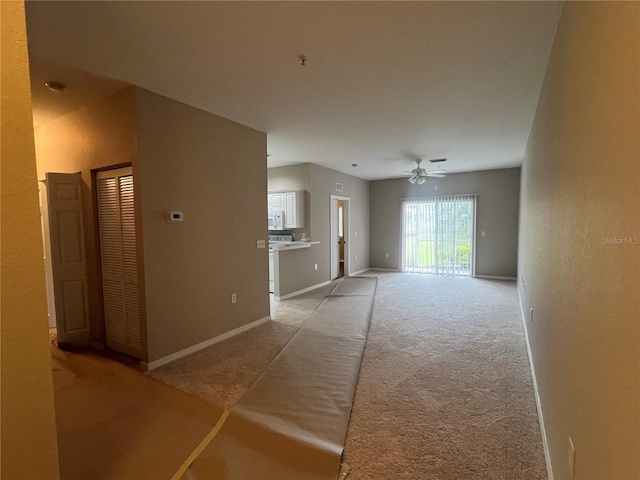 unfurnished living room featuring light carpet, baseboards, and a ceiling fan