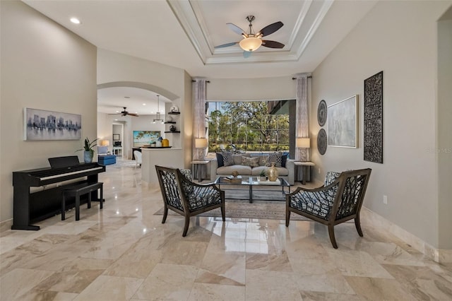 living area featuring a ceiling fan, a tray ceiling, arched walkways, ornamental molding, and marble finish floor