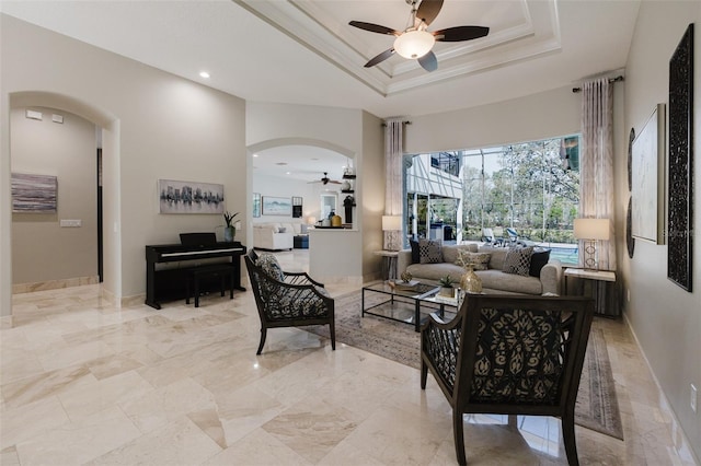 living room with baseboards, ceiling fan, ornamental molding, arched walkways, and a raised ceiling