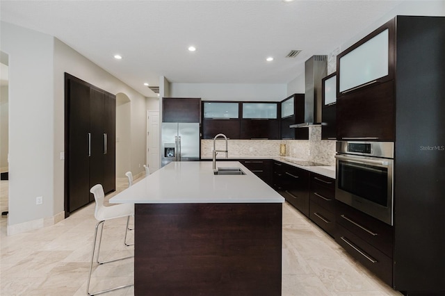 kitchen featuring a sink, light countertops, appliances with stainless steel finishes, wall chimney exhaust hood, and backsplash