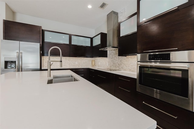 kitchen with visible vents, wall chimney range hood, light countertops, appliances with stainless steel finishes, and a sink