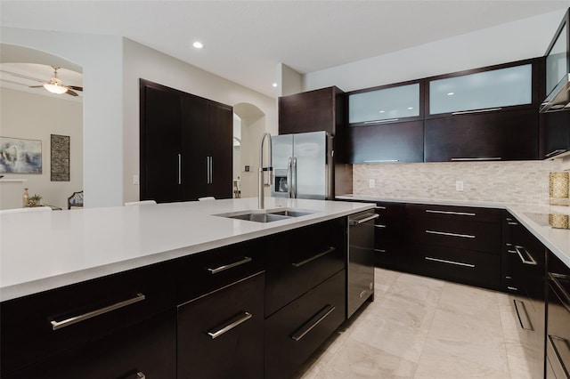 kitchen featuring a sink, tasteful backsplash, arched walkways, appliances with stainless steel finishes, and light countertops